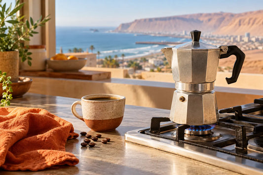 Cafetera moka italiana sobre fuego bajo junto a una taza de café con vista a la costa de Arica